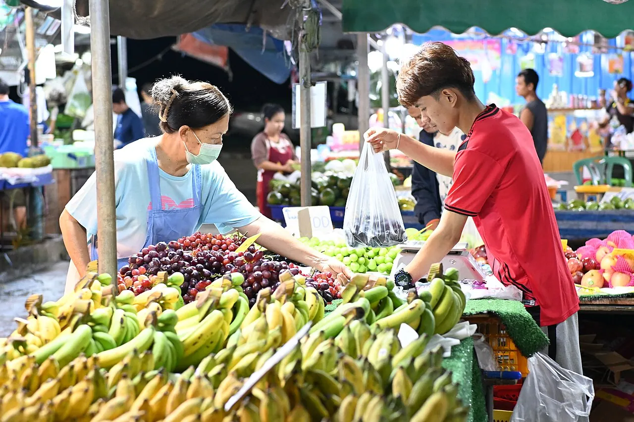 A stallholder hands a bag of fruit across the counter